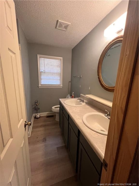 bathroom featuring toilet, visible vents, a sink, and wood finished floors