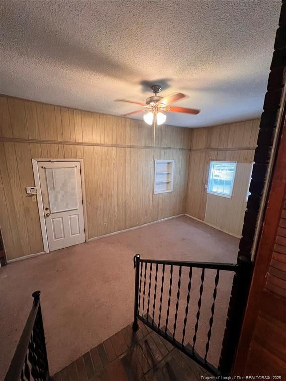 interior space featuring wood walls, carpet, ceiling fan, and a textured ceiling