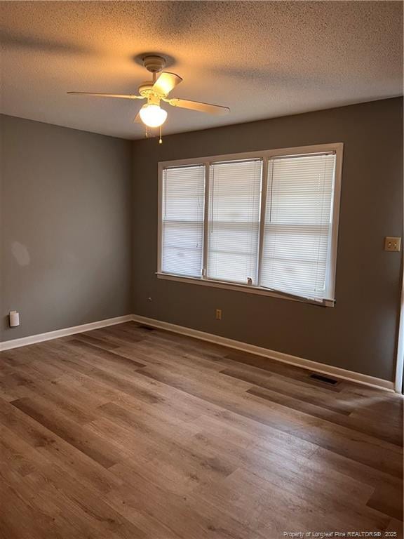 unfurnished room with a wealth of natural light, visible vents, baseboards, and wood finished floors