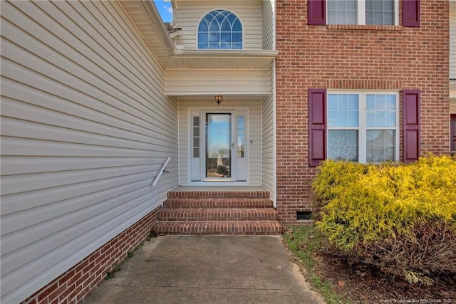 view of exterior entry featuring brick siding and crawl space