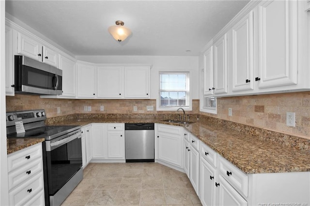 kitchen featuring stainless steel appliances, backsplash, white cabinets, a sink, and dark stone counters