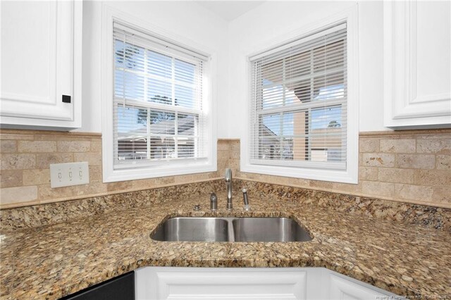 kitchen with dark stone countertops, white cabinetry, and a sink