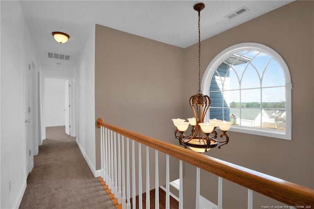 hall with carpet, visible vents, baseboards, and an inviting chandelier