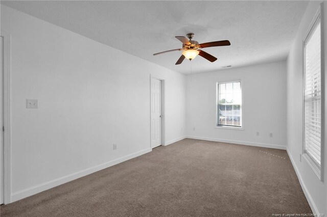 carpeted spare room featuring a ceiling fan and baseboards