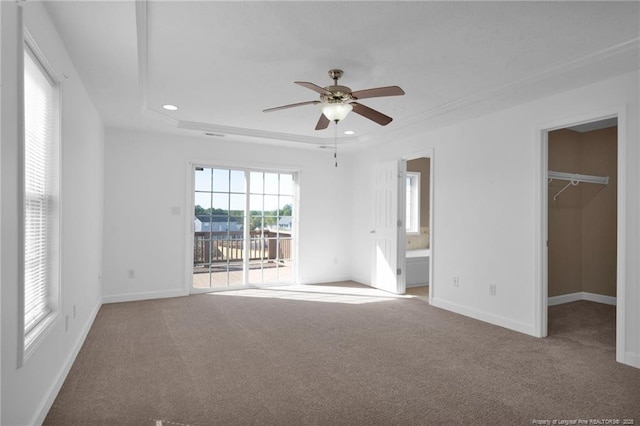 unfurnished bedroom featuring access to exterior, a tray ceiling, a walk in closet, carpet floors, and baseboards