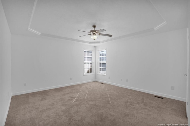 empty room featuring carpet floors, a tray ceiling, visible vents, ceiling fan, and baseboards