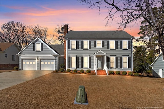 colonial home with driveway, an attached garage, and a chimney