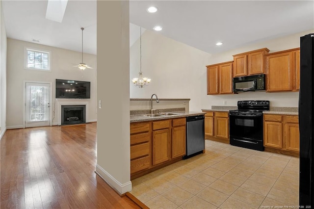 kitchen with a fireplace, a sink, a ceiling fan, brown cabinets, and black appliances