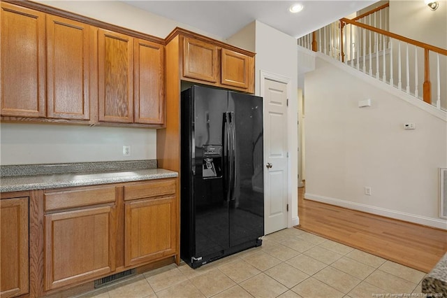 kitchen with light tile patterned floors, visible vents, black fridge with ice dispenser, brown cabinets, and light countertops