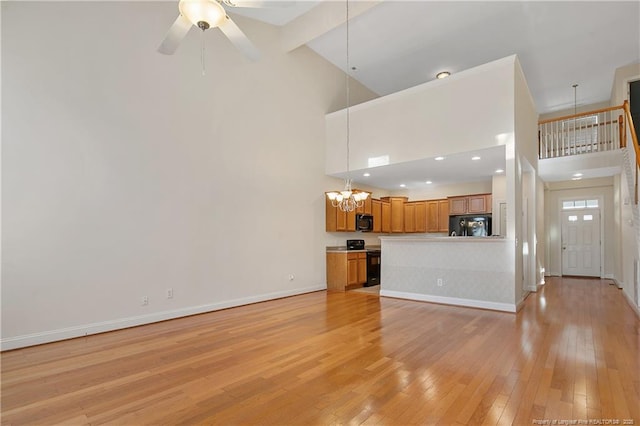 unfurnished living room with high vaulted ceiling, light wood-style flooring, baseboards, and ceiling fan with notable chandelier