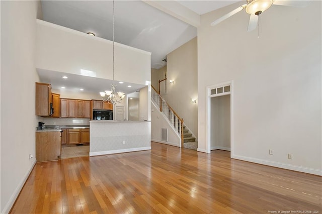 unfurnished living room with beam ceiling, light wood-style floors, high vaulted ceiling, baseboards, and stairs