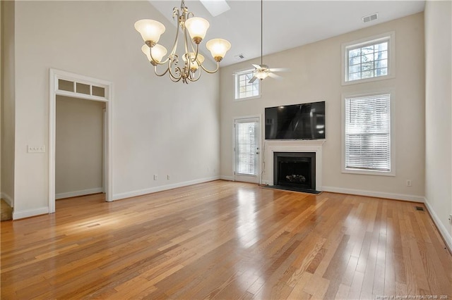 unfurnished living room with visible vents, a healthy amount of sunlight, a towering ceiling, light wood-type flooring, and a fireplace