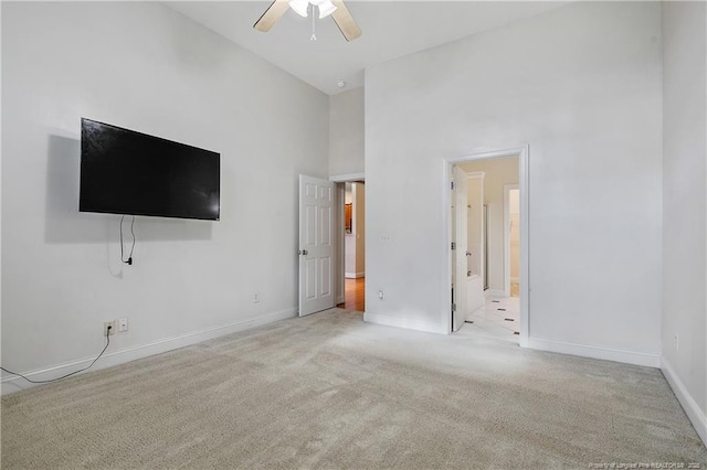 interior space featuring ceiling fan, a high ceiling, baseboards, and carpet flooring