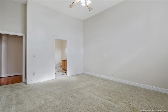 unfurnished bedroom featuring a high ceiling, a ceiling fan, light carpet, ensuite bath, and baseboards