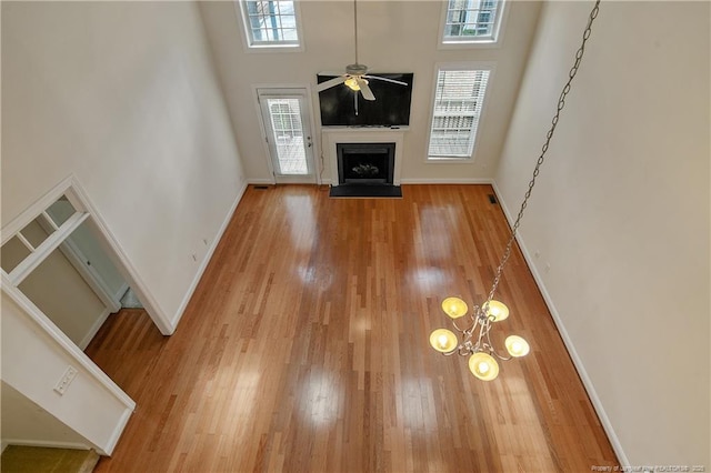 unfurnished living room with baseboards, a towering ceiling, a fireplace with flush hearth, ceiling fan, and wood finished floors