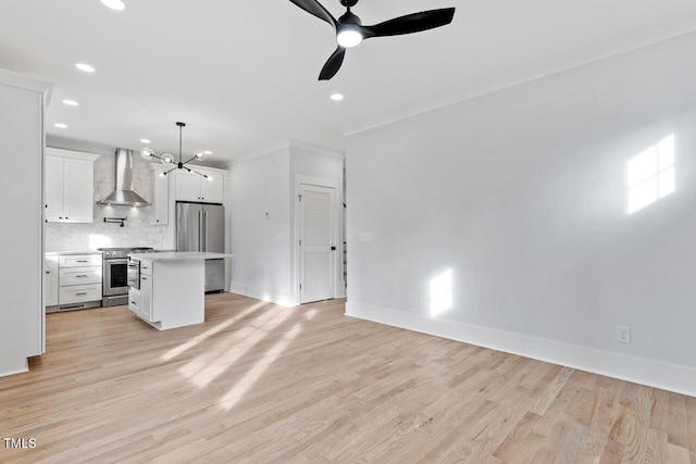 kitchen featuring backsplash, wall chimney range hood, light countertops, light wood-style flooring, and appliances with stainless steel finishes