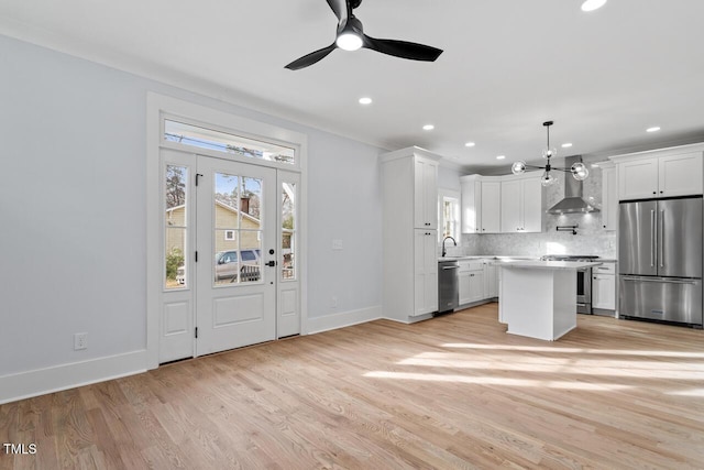 kitchen with light countertops, decorative backsplash, light wood-style flooring, appliances with stainless steel finishes, and wall chimney exhaust hood