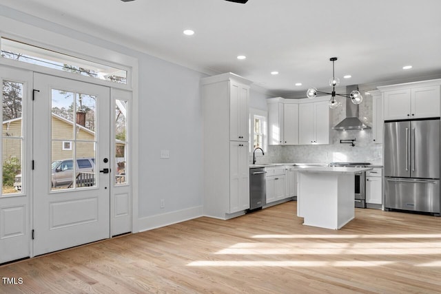 kitchen featuring decorative backsplash, light wood-style floors, appliances with stainless steel finishes, white cabinetry, and wall chimney exhaust hood