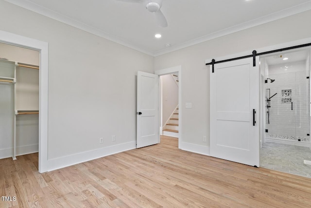 unfurnished bedroom with a barn door, a spacious closet, light wood-style floors, and ornamental molding