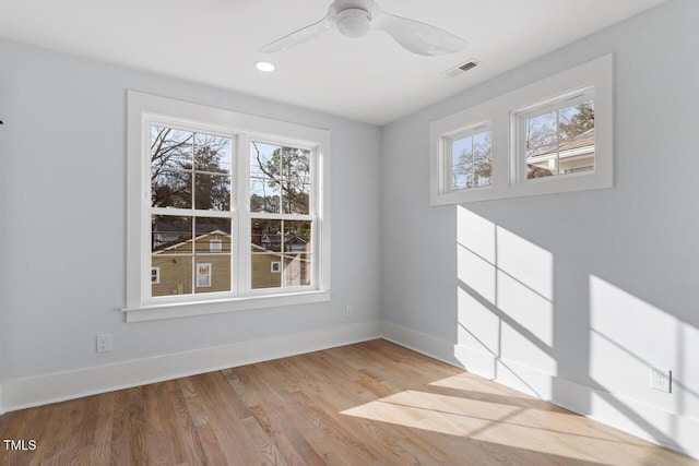 empty room featuring ceiling fan, visible vents, baseboards, and wood finished floors