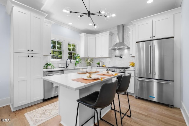kitchen with wall chimney range hood, high quality appliances, white cabinets, and decorative backsplash