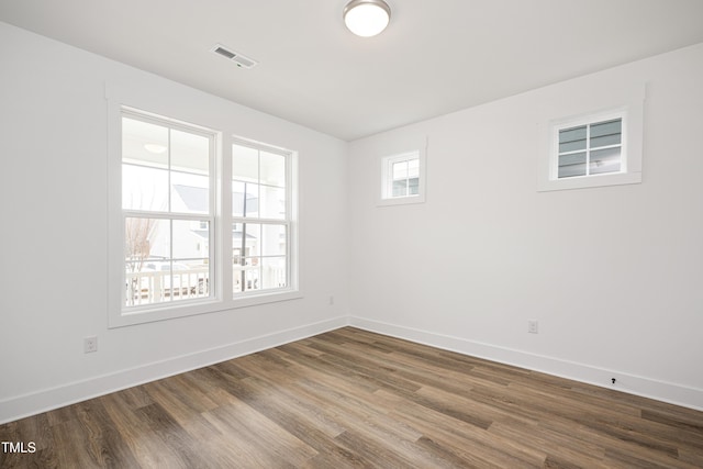 empty room featuring baseboards, visible vents, and dark wood-style flooring