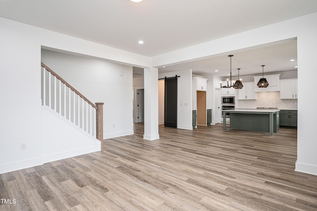 unfurnished living room featuring a barn door, baseboards, light wood-style flooring, stairs, and recessed lighting