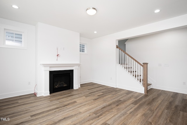 unfurnished living room with a fireplace, recessed lighting, stairway, wood finished floors, and baseboards