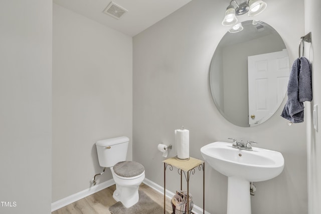 half bath featuring visible vents, toilet, a sink, wood finished floors, and baseboards