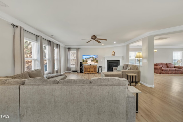 living room featuring a glass covered fireplace, baseboards, crown molding, and light wood finished floors