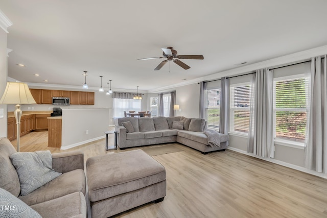 living area with light wood-style flooring, baseboards, crown molding, and ceiling fan with notable chandelier