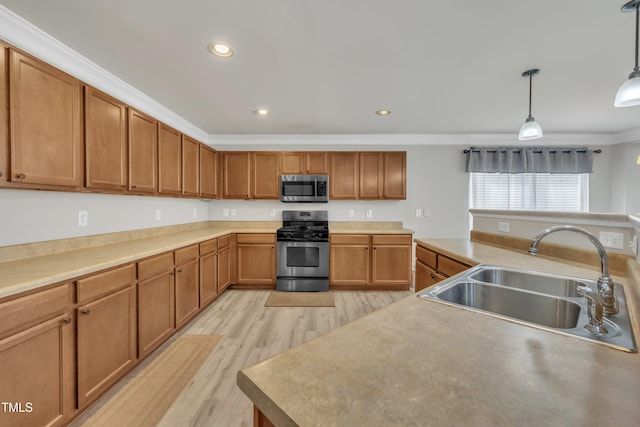 kitchen with appliances with stainless steel finishes, ornamental molding, hanging light fixtures, light wood-style floors, and a sink