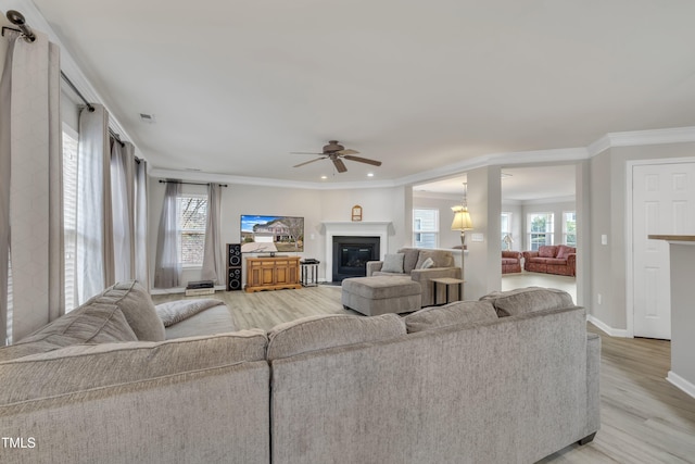 living room with ornamental molding, a glass covered fireplace, a wealth of natural light, and light wood-style floors