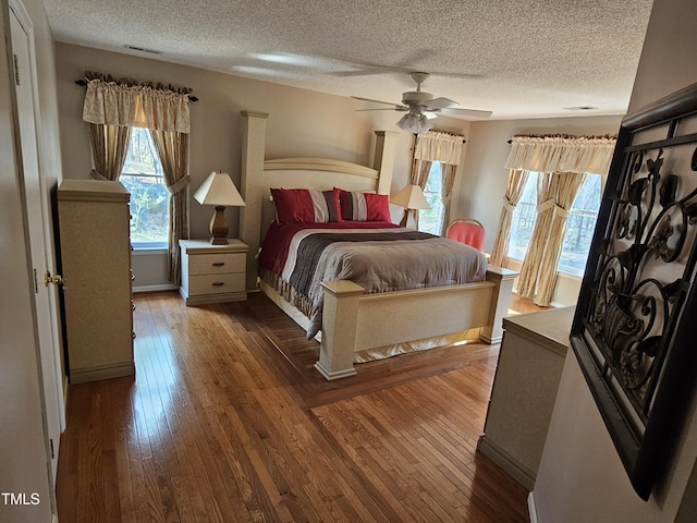 bedroom featuring dark wood-style floors, visible vents, a textured ceiling, and ceiling fan