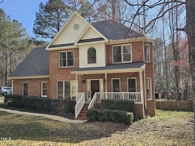 view of front of home with brick siding, covered porch, and roof with shingles