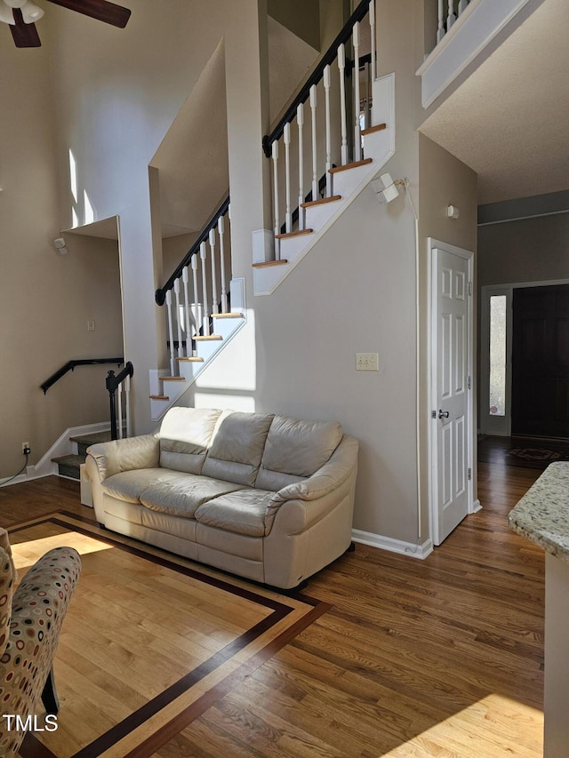 living area with stairway, wood finished floors, baseboards, and a towering ceiling