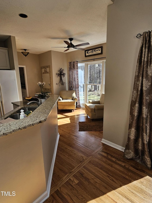 unfurnished living room with dark wood-style floors, baseboards, ceiling fan, a sink, and a textured ceiling