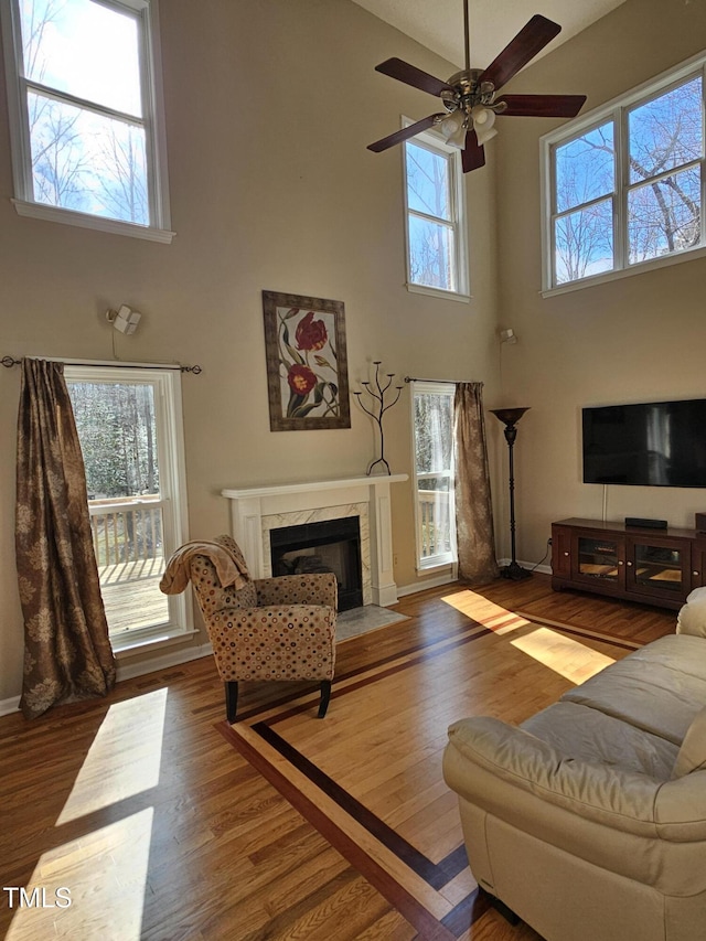 living area with a premium fireplace, baseboards, wood finished floors, and a ceiling fan