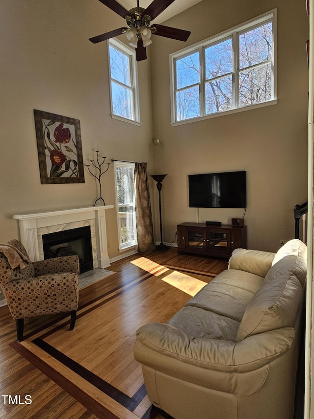 living room with wood finished floors, baseboards, a premium fireplace, a high ceiling, and ceiling fan