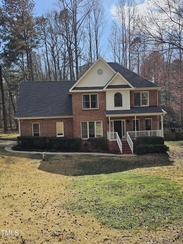 view of front of house with brick siding, covered porch, a shingled roof, and a front lawn