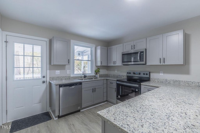 kitchen featuring light stone counters, stainless steel appliances, light wood-style flooring, gray cabinetry, and a sink