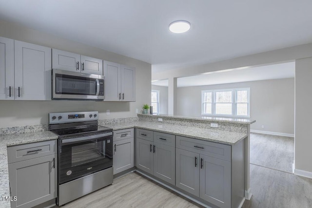 kitchen with stainless steel appliances, light wood-style floors, a peninsula, and gray cabinetry