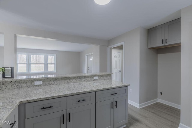 kitchen featuring light wood-type flooring, baseboards, light stone counters, and gray cabinets