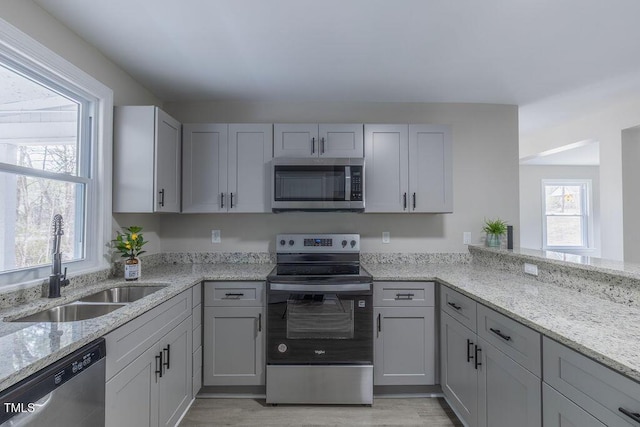 kitchen with light wood-type flooring, light stone countertops, stainless steel appliances, and a sink