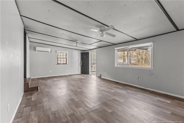 unfurnished room featuring a wall unit AC, ceiling fan, baseboards, and wood finished floors