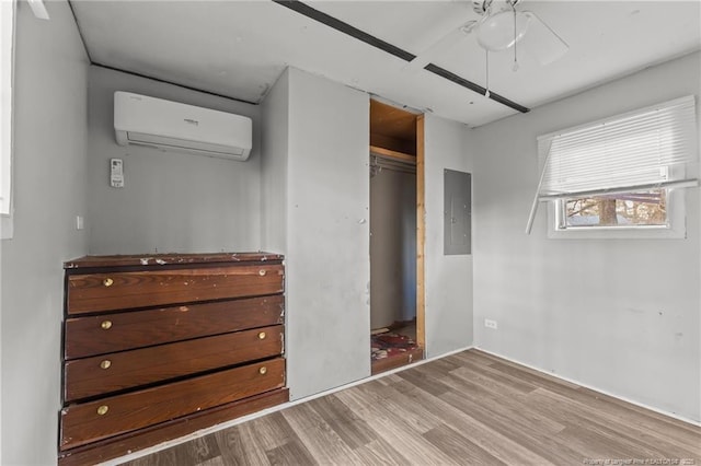 unfurnished bedroom featuring wood finished floors, a ceiling fan, an AC wall unit, a closet, and electric panel