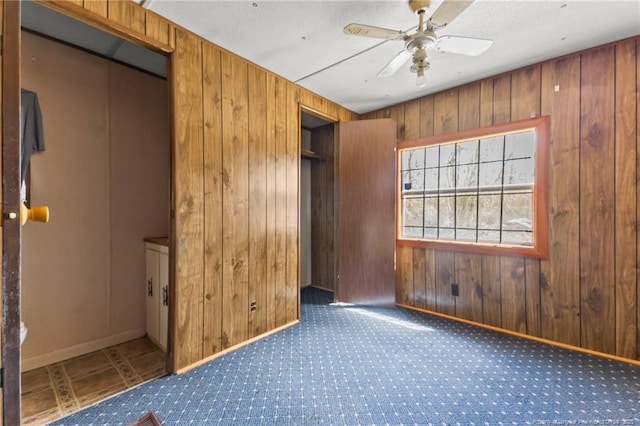 carpeted spare room with a ceiling fan, wood walls, and baseboards