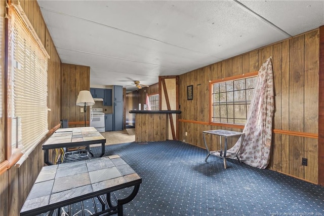 living area with carpet floors, a ceiling fan, and wooden walls