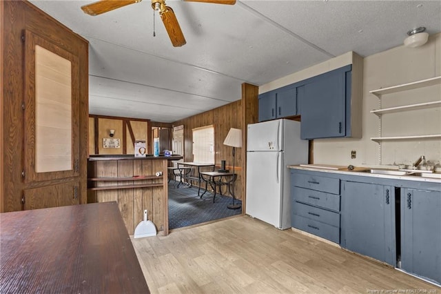 kitchen featuring a ceiling fan, light wood-style flooring, freestanding refrigerator, blue cabinetry, and a sink