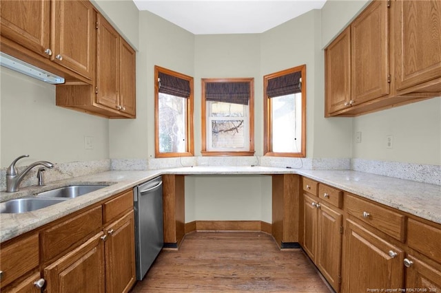 kitchen with brown cabinetry, a sink, light wood finished floors, and stainless steel dishwasher